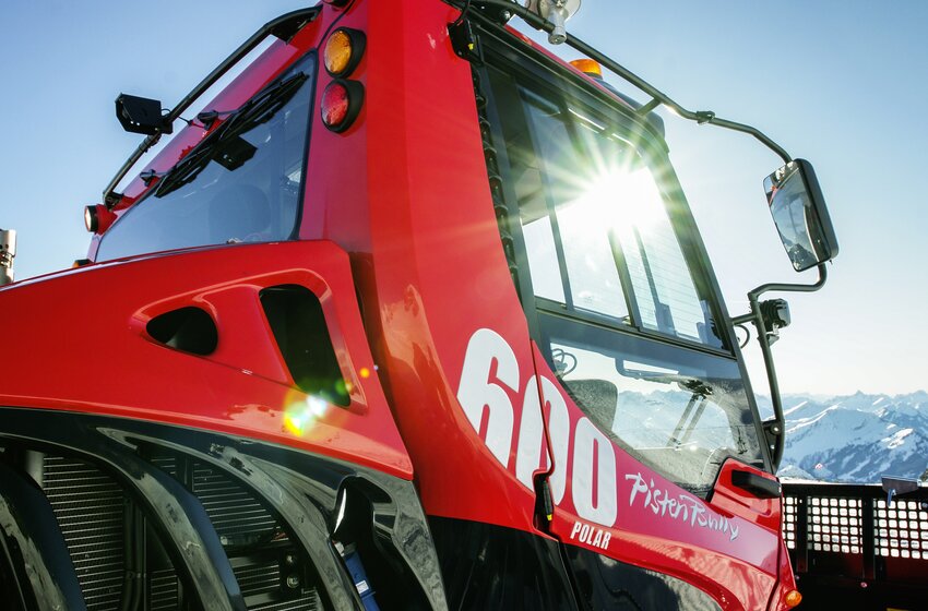 Nahaufnahme der roten PistenBully 600 Polar Raupe mit Sonne und Alpenkulisse | © Hochkönig Bergbahnen GmbH