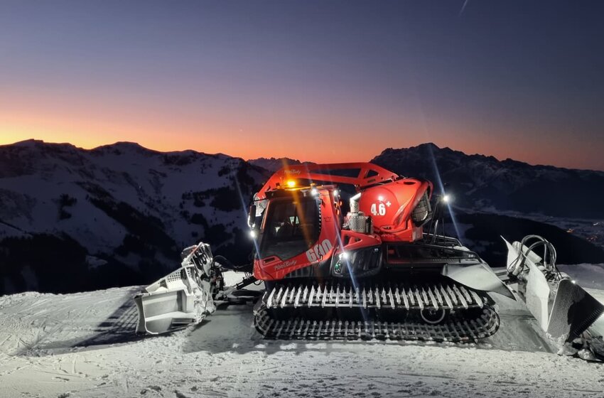 Rote Pistenraupe auf verschneiter Bergkuppe bei Sonnenuntergang, umgeben von Alpenpanorama | © Hochkönig Bergbahnen GmbH