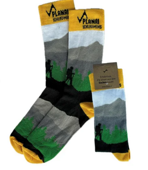 Drei Paar Wandersocken mit Planai-Schriftzug, Berglandschaft, Wanderern und grün-gelbem Design | © Planai-Hochwurzen-Bahnen GmbH