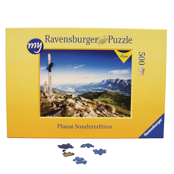 Puzzlebox zeigt felsigen Gipfel der Planai mit Holzkreuz und Blick auf grüne Täler und Berge im Sommer | © Planai-Hochwurzen-Bahnen GmbH