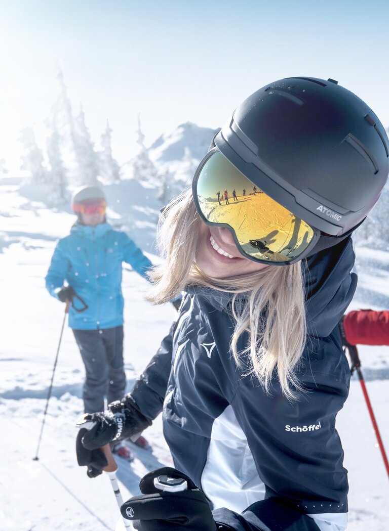 Drei Skifahrer stehen lachend im Schnee, eine Frau im Vordergrund lächelt in die Kamera, Sonne und Berge im Hintergrund. | © Ski amadé GmbH